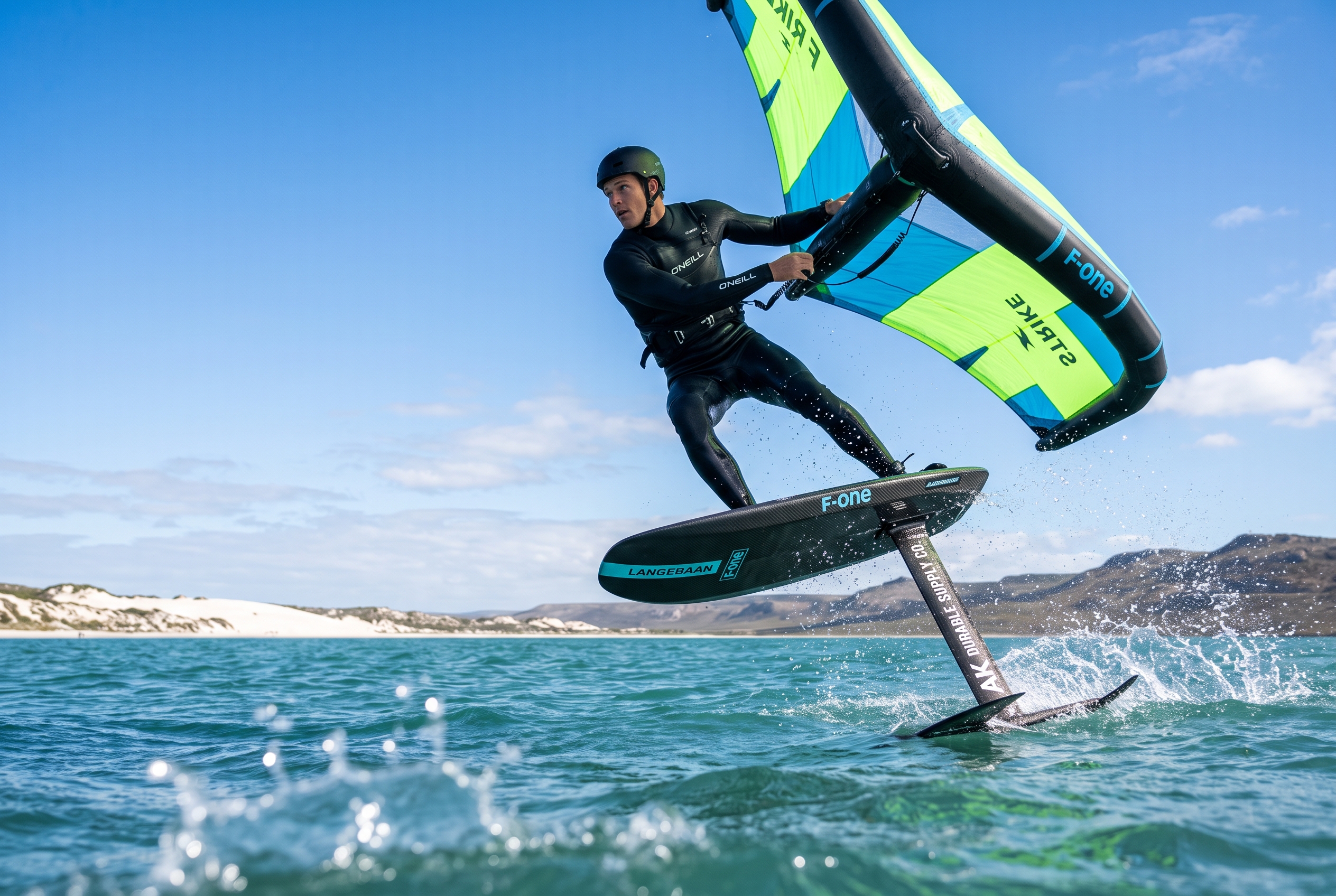 Wing foiler in a wetsuit riding a hydrofoil across the flat blue water of Langebaan Lagoon, South Africa