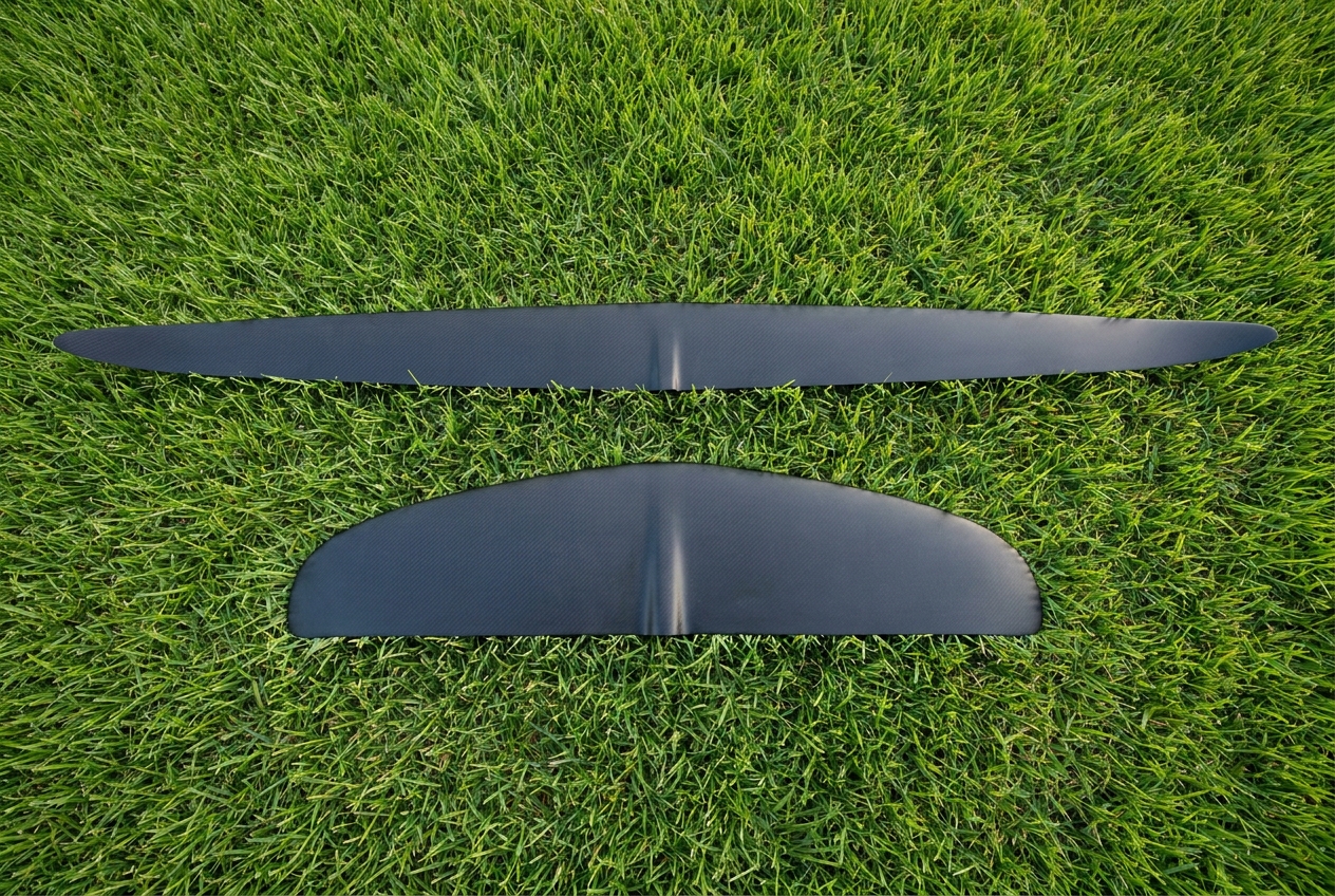 A long, slender high aspect hydrofoil front wing laid on grass above a shorter, much deeper low aspect front wing, showing the contrast in wingspan and chord