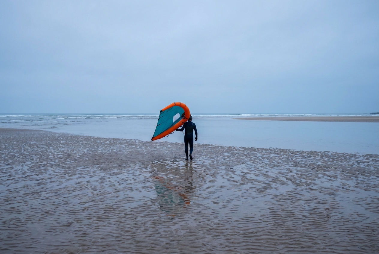 Illustration of a wing foiler carrying an inflatable wing across a sandy beach launch toward flat estuary water at Hayling Island